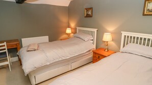 A bedroom with two beds, a nightstand, a chair, and a radiator. - Firkin Cottage (Bedale)
