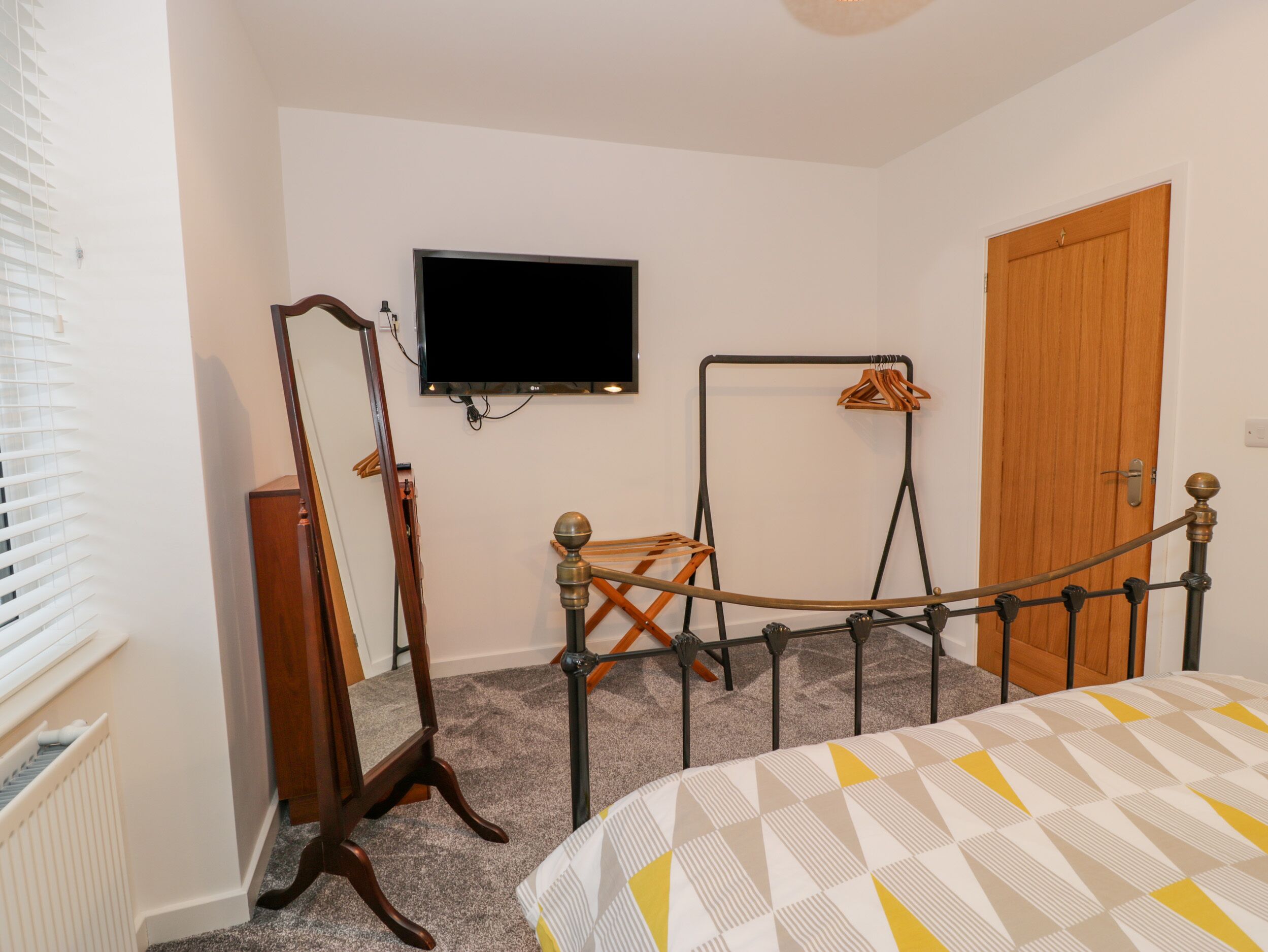 Una camera da letto con un letto, un armadio in legno, uno specchio, una televisione a muro e una porta.