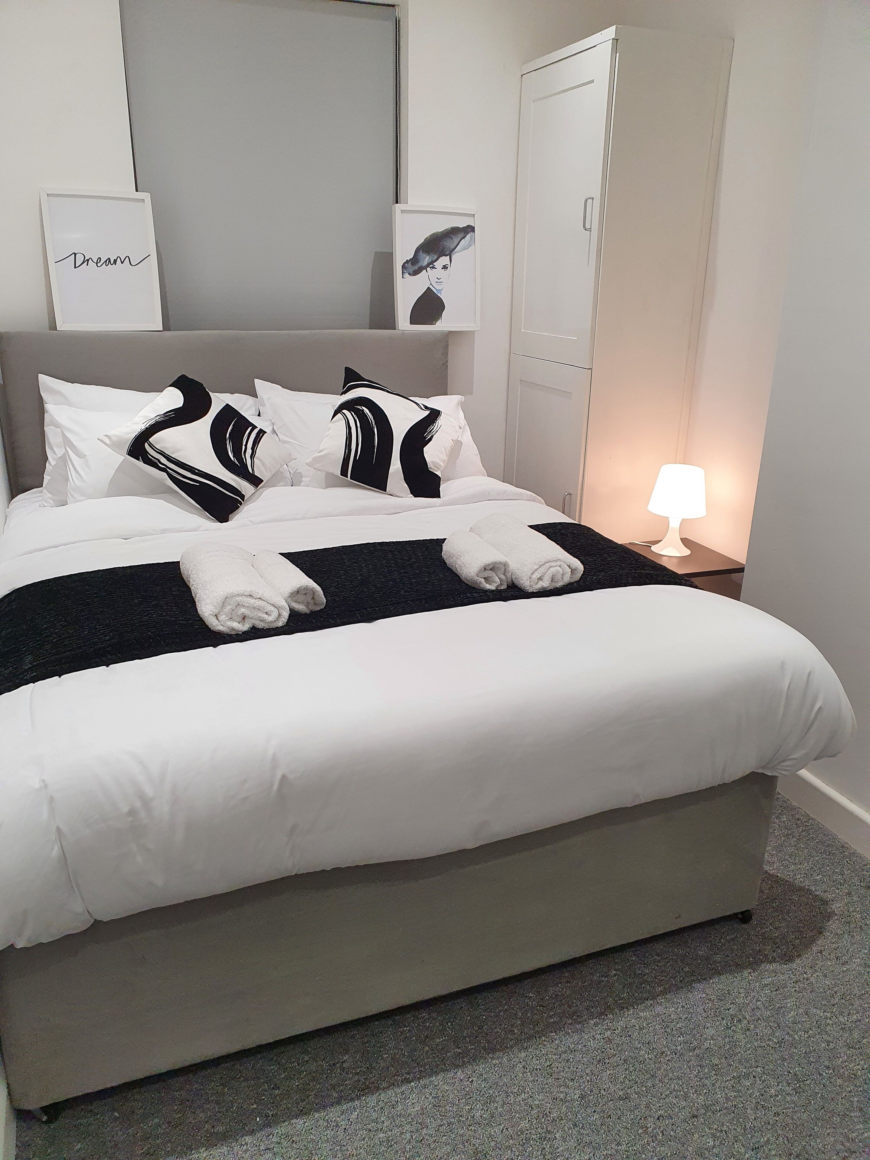 A neatly made bed with white and black bedding, a folded towel, and a bedside lamp.