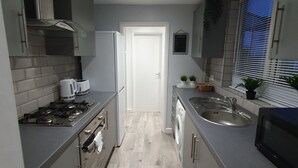 A narrow kitchen with grey cabinets, a stainless steel sink, a microwave, and a stove. - “Family-Friendly Fun: Spacious Home Near Top Attractions” (Ironville)