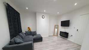 A modern living room with a sectional sofa, a flat-screen TV mounted on the wall, and a large mirror. - “Family-Friendly Fun: Spacious Home Near Top Attractions” (Ironville)