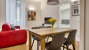 Un salon moderne avec un canapé rouge, une table à manger en bois et des chaises, un téléviseur et des œuvres d’art accrochées aux murs.