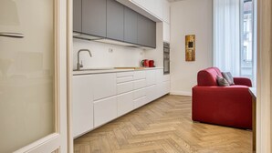 Une cuisine moderne avec des meubles blancs, un canapé rouge et un parquet à motifs en chevrons.