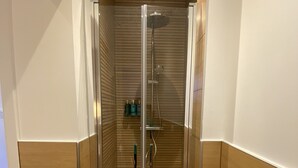 A modern shower enclosure with a glass door, wooden paneling, and a built-in shelf with toiletries. - Appart Privé Deluxe Strasbourg City (Strasbourg)