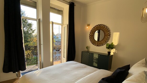 A bedroom with a large bed, a dresser, a mirror, and a balcony with curtains. - Appart Privé Deluxe Strasbourg City (Strasbourg)