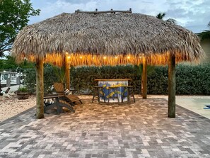 A thatched gazebo with a table and chairs underneath, surrounded by a paved patio area.