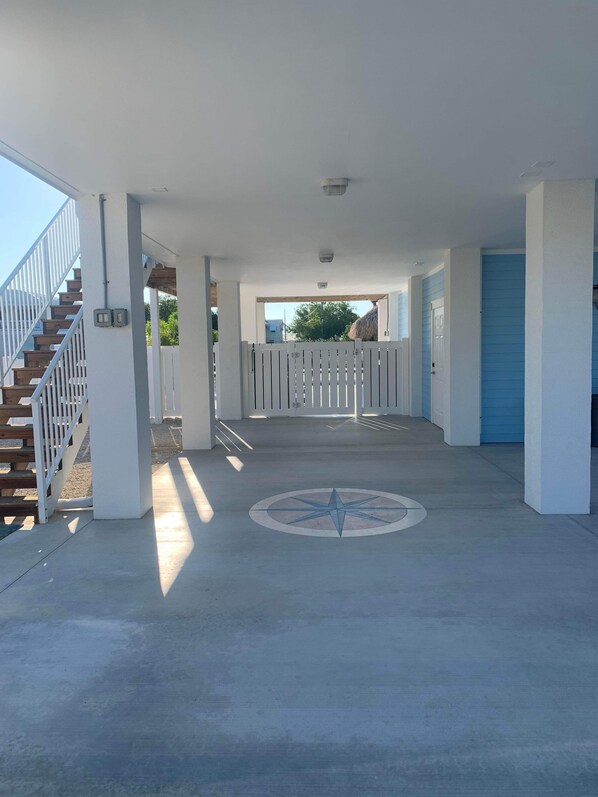 A covered outdoor area with a concrete floor, a white fence, and a wooden staircase on the left.