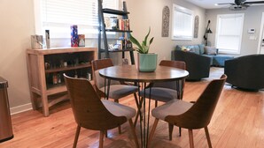 A dining area with a round table, four chairs, a bookshelf, and a potted plant.