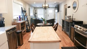 A modern kitchen with a central island, wooden cabinets, a built-in oven, and a dining area with chairs and a table.