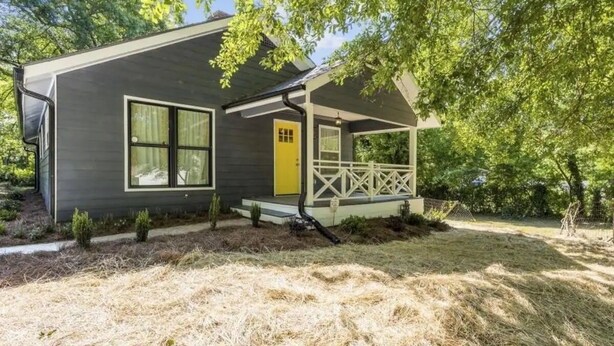 A single-story house with a porch, a yellow door, and a fenced yard.