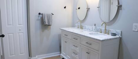 A bathroom with white cabinetry, a sink with gold fixtures, and two wall-mounted mirrors.