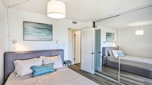 Een slaapkamer met een bed, nachtkastje, lamp en een grote spiegel.
