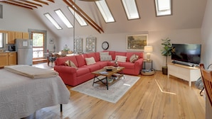 A spacious loft with a red sofa, wooden beams, skylights, a TV, and a kitchen area.