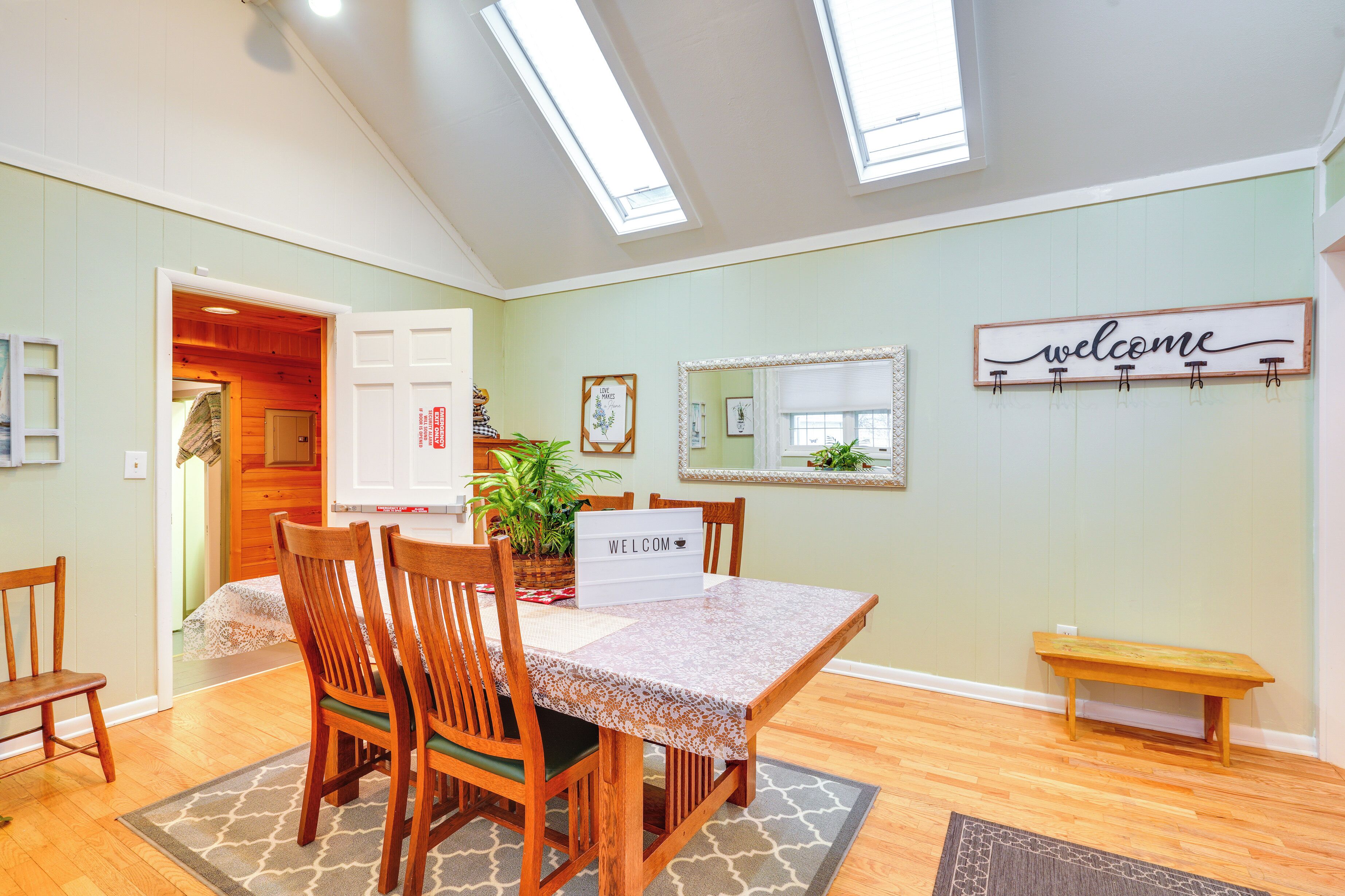A dining area with a wooden table and chairs, a 'welcome' sign, a mirror, and a bench.