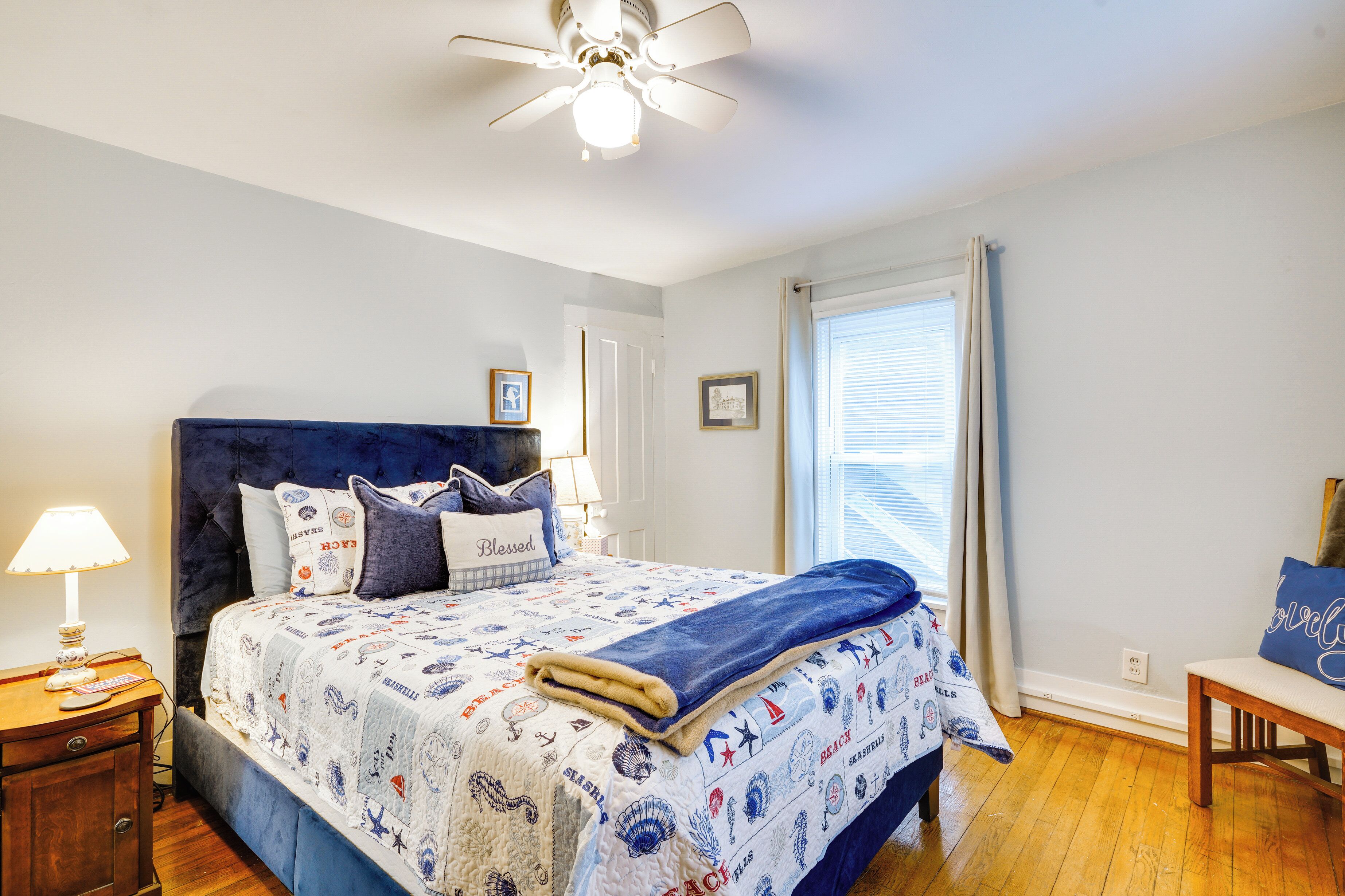 A bedroom with a bed, a nightstand, a chair, a ceiling fan, and a window with curtains.