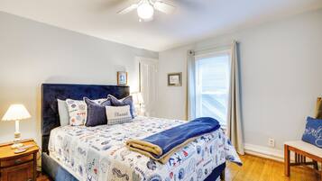 A bedroom with a bed, a nightstand, a chair, a ceiling fan, and a window with curtains.