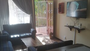 A living room with a sofa, a TV, a table, and a door leading outside.