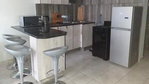 A modern kitchen with a central island, bar stools, a microwave, a coffee maker, and a refrigerator.