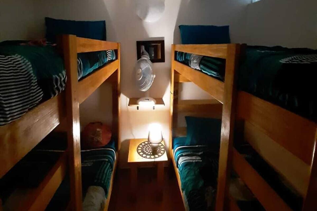 Ein Schlafsaalzimmer mit Etagenbetten, einem kleinen Tisch mit Lampe und einem Deckenventilator.