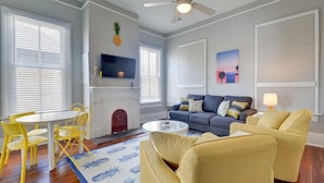 A living room with a fireplace, yellow chairs, a gray sofa, and a ceiling fan. - Beauty on Ball - Main 2 - King Bed, Near restaurants and beach!! (Galveston)