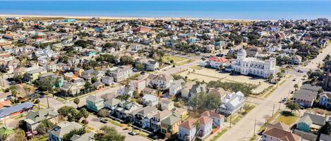 Vista aérea de una zona residencial costera con casas, un gran edificio blanco con cúpula y una playa al fondo.