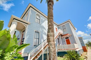 A two-story house with a white picket fence, a red door, and a staircase leading to the second floor. - Beauty on Ball - Main 2 - King Bed, Near restaurants and beach!! (Galveston)