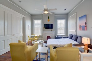 A hotel room with a bed, two yellow armchairs, a small table, a ceiling fan, a fireplace, and a TV mounted on the wall. - Beauty on Ball - Main 2 - King Bed, Near restaurants and beach!! (Galveston)