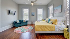 A bedroom with a bed, a blue sofa, a ceiling fan, and two windows with blinds. - Beauty on Ball - Main 2 - King Bed, Near restaurants and beach!! (Galveston)