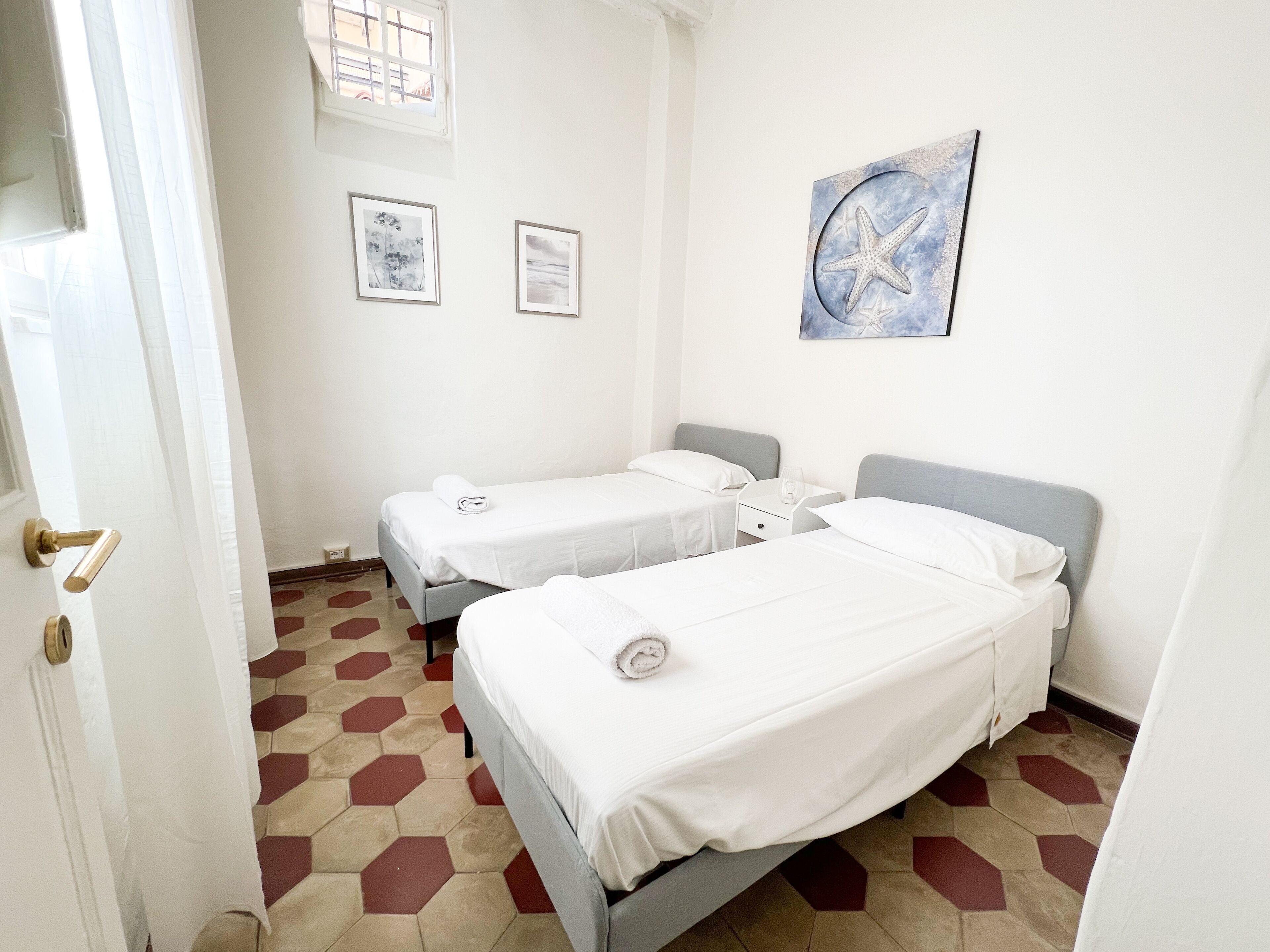 Hotellihuone, jossa on kaksi erillistä sänkyä, pieni yöpöytä lasilla ja seinälle kiinnitetty taideteos.