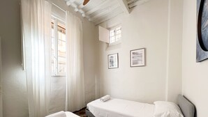 Una camera da letto con due letti singoli, una finestra con tende leggere e due quadri appesi al muro.