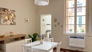 Un'area pranzo con tavolo e sedie bianche, una lampada a sospensione bianca, una finestra con vista sull'esterno e un termosifone a parete.