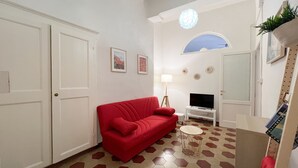 Un soggiorno con un divano rosso, una TV, una lampada e un tavolino rotondo.