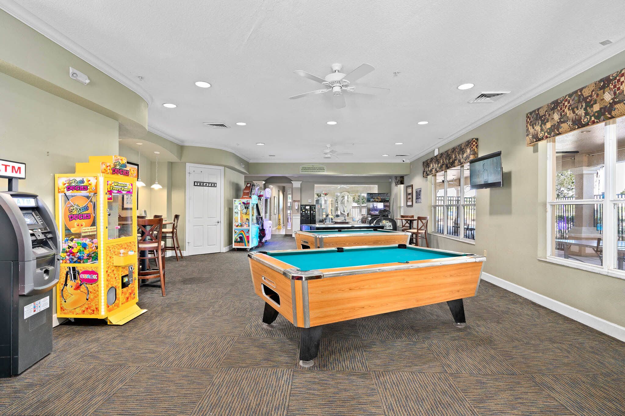 A pool table in a room with carpeted flooring, a ceiling fan, and vending machines.