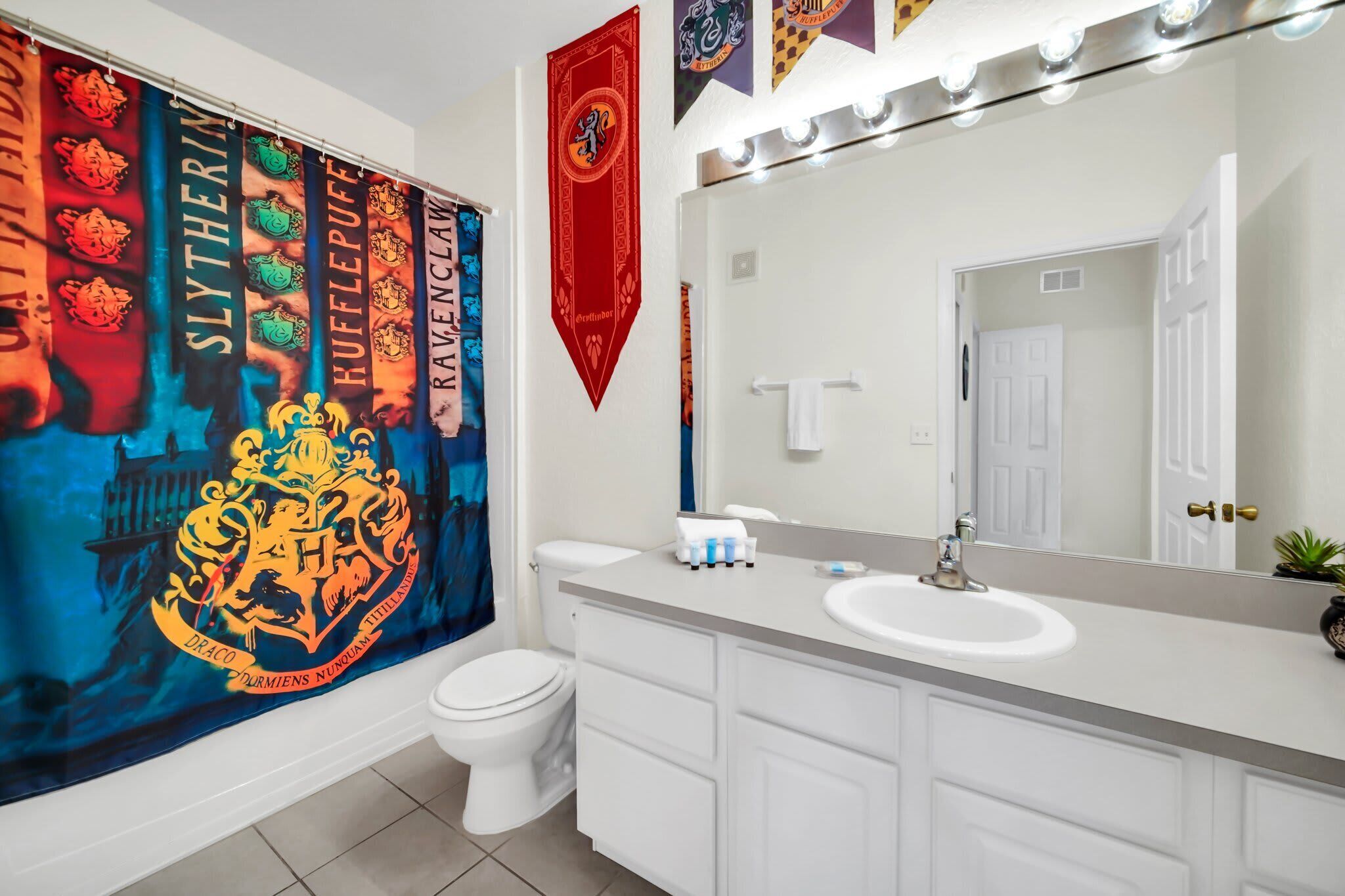 A bathroom with a white sink, mirror, and white cabinets. There are banners on the wall and a towel hanging on the door.