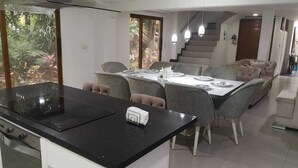 A modern kitchen with a black countertop, white cabinets, and a built-in stove. There is a dining area with a table and chairs, and a staircase leading to another level. - CASA SUYTE LEGUIZAMON (Envigado)