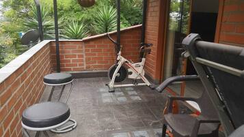 A covered outdoor area with a brick wall, a stationary exercise bike, and two round tables.