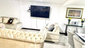 A living room with a large beige sofa, a smaller sofa, a TV mounted on the wall, and a framed picture above a table with chairs. - CASA SUYTE LEGUIZAMON (Envigado)
