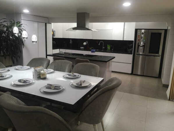 Una cucina moderna con zona pranzo, che include un'isola centrale, sedie grigie e un frigorifero in acciaio inossidabile.