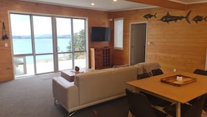 A cozy room with a large sliding glass door leading to a scenic view, a wooden dining table with chairs, a sofa, and a flat-screen TV mounted on the wall.