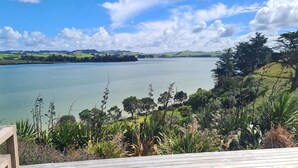 A lakeside view with a wooden deck, lush greenery, and distant hills.
