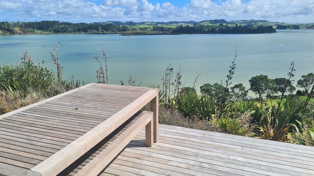 A wooden deck with a bench overlooking a lake and distant hills.