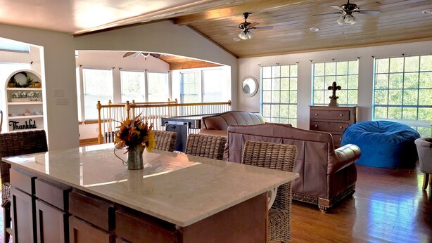A spacious living area with a large island table, wicker furniture, and a ceiling fan.