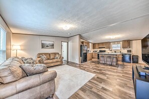 A spacious living room with a large sofa and a kitchen area featuring wooden flooring and modern appliances.
