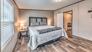 Un dormitorio con cama, lámparas de noche, mesita de noche, suelo de madera y una puerta que da a otra habitación.