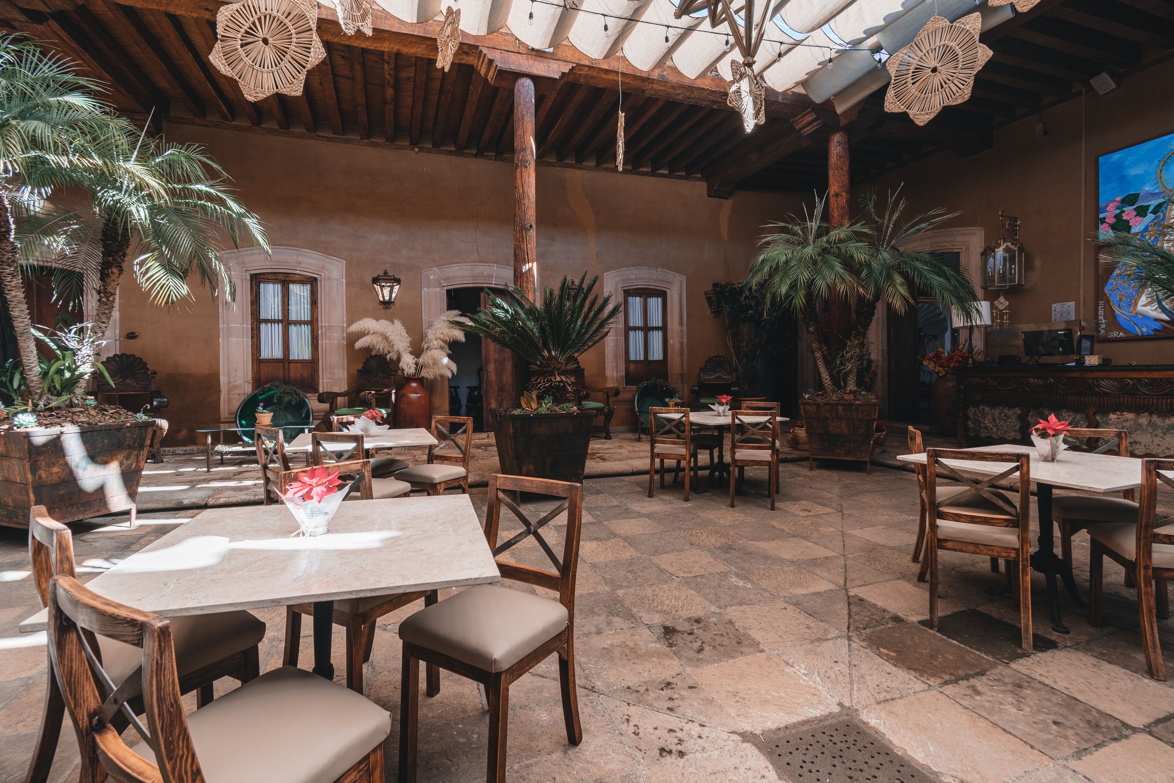 An outdoor café with wooden tables and chairs, potted plants, and a rustic ceiling.