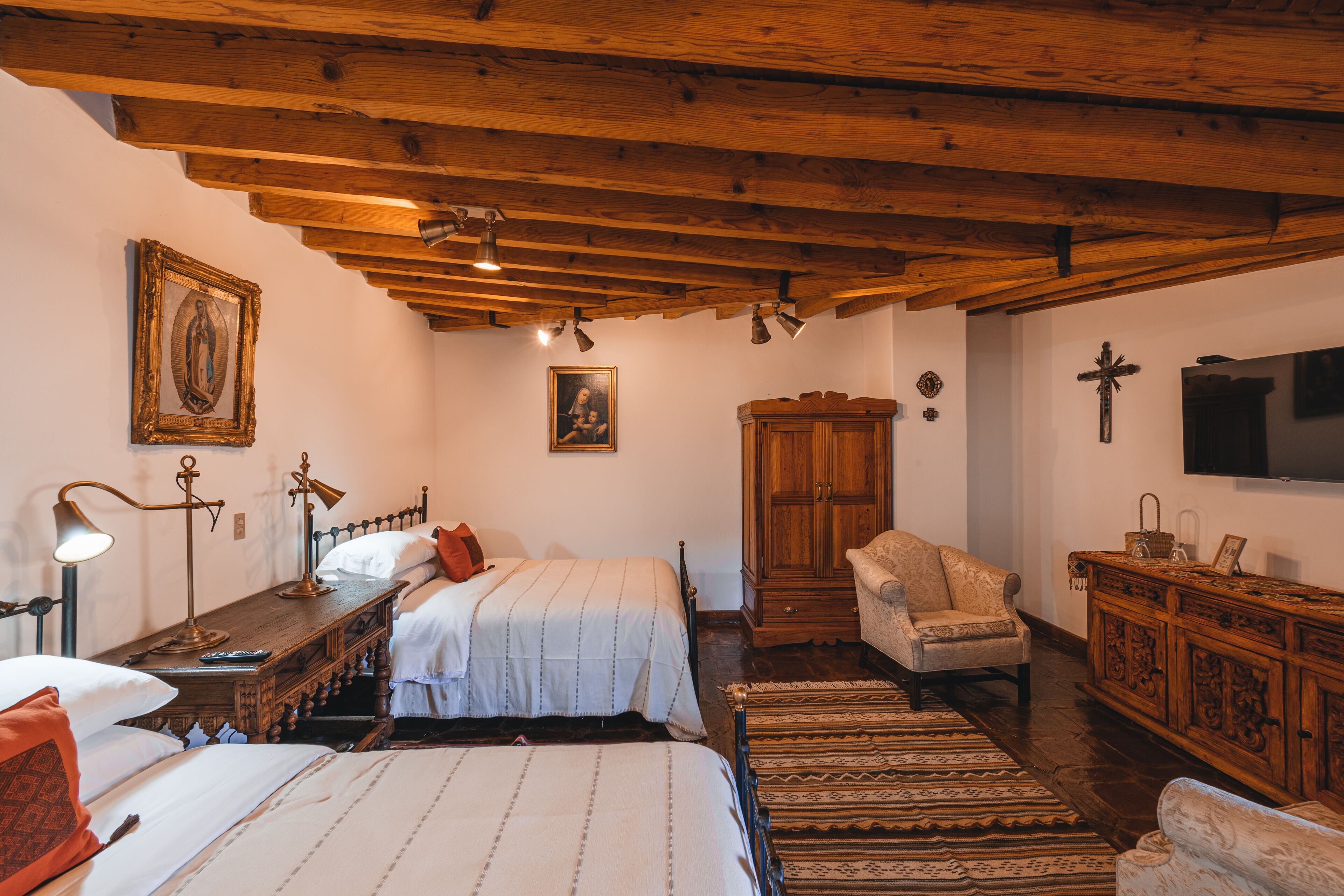 A room with wooden beams, a bed with white bedding, a wooden cabinet, and a television on the wall.