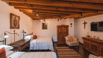 A room with wooden beams, a bed with white bedding, a wooden cabinet, and a television on the wall.