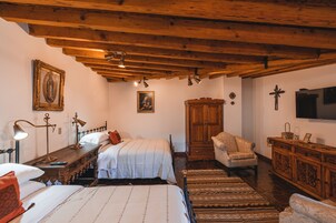 A room with wooden beams, a bed with white bedding, a wooden cabinet, and a television on the wall.