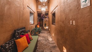 A narrow hallway with a wooden bench, colorful cushions, a stone pathway, and a sign indicating an evacuation route.