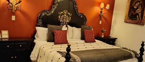 Una habitación tradicional con techo de madera, una cama grande con cabecera oscura, múltiples almohadas y dos lámparas de pared.